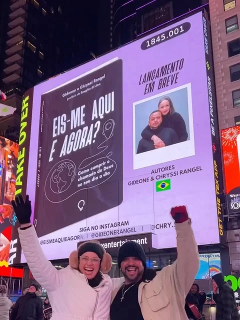 Gideone e Chryssi Rangel comemorando diante do telão da Times Square com a capa de Eis-me Aqui e Agora?